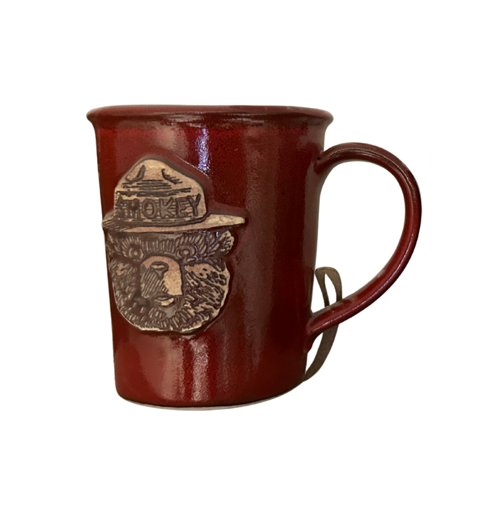 Smokey Bear stoneware mug in a deep forest fire red glaze with hand-carved Smokey Bear ranger hat medallion